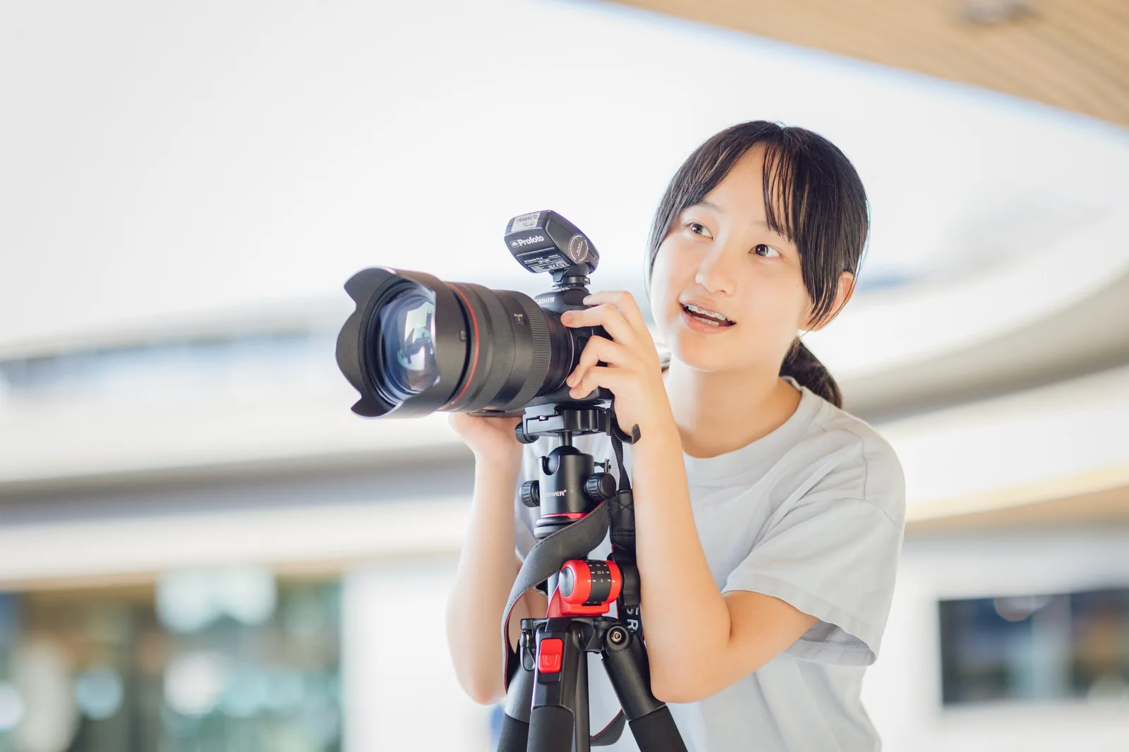 三脚に固定したプロ用カメラを構えて、笑顔で被写体を見つめる子ども