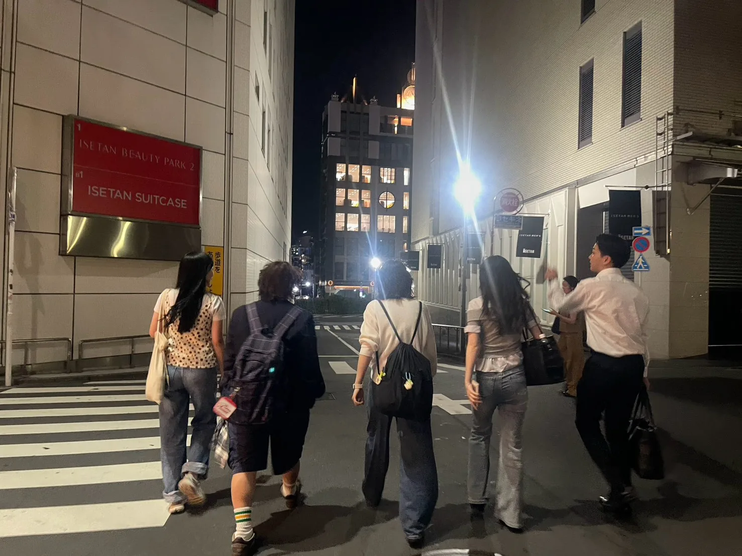 夜の街を、メンバー5人が並んで歩いていく後ろ姿